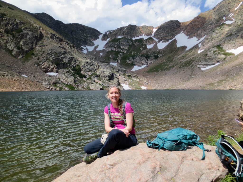 Nicky sitting on a rock with lake and mountains in background